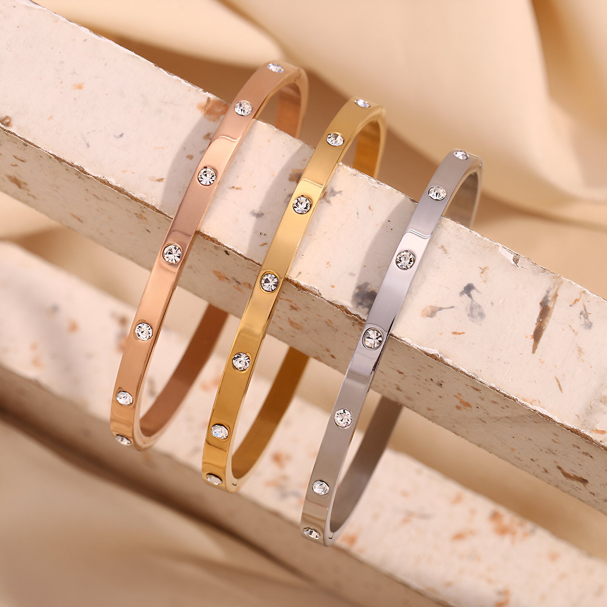 Trois bracelets jonc fins en acier inoxydable, couleurs or rosé, or jaune et argent, ornés de petits éclats brillants.