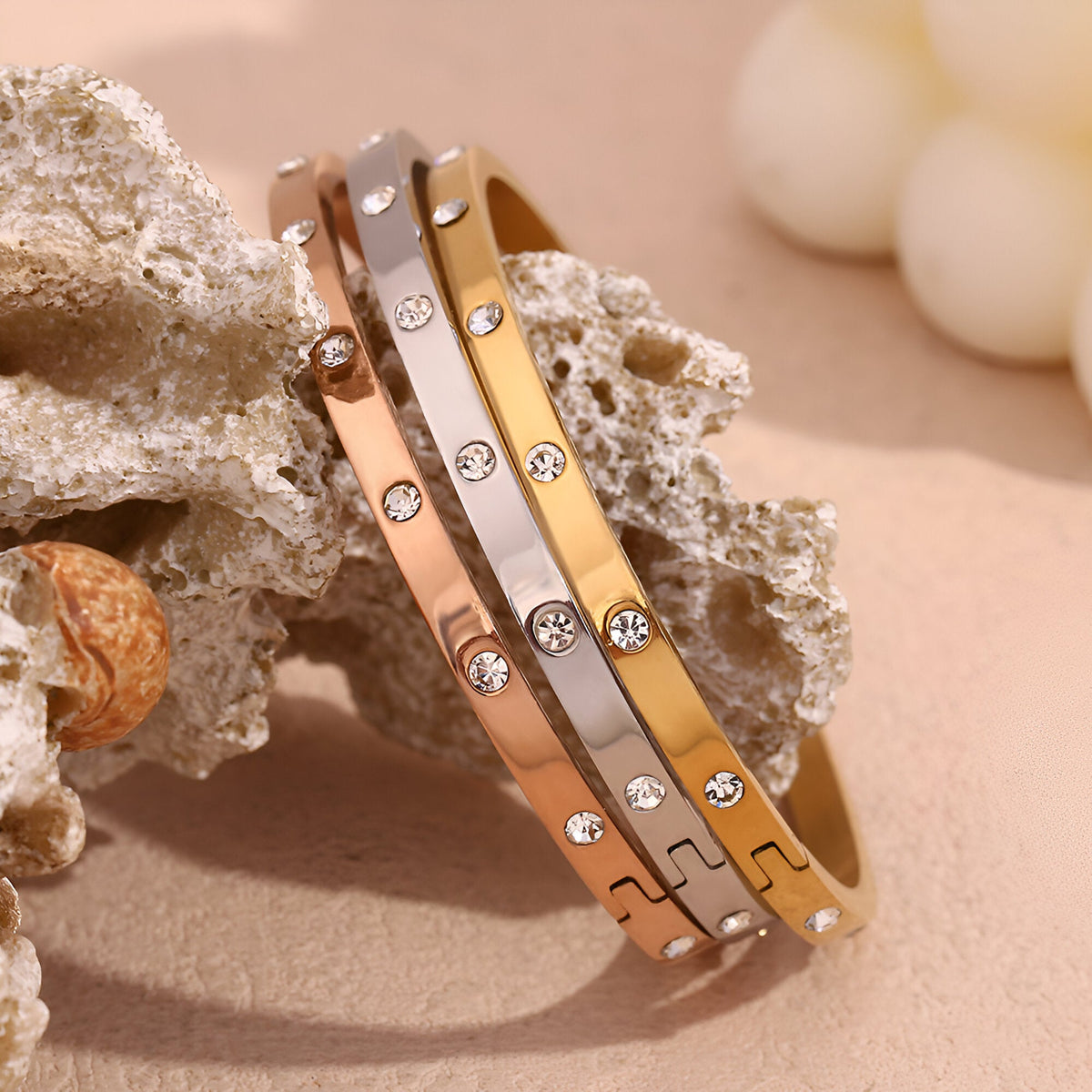 Trois bracelets joncs en acier inoxydable or, or rosé et argent avec éclats de lumière sertis de cristaux.