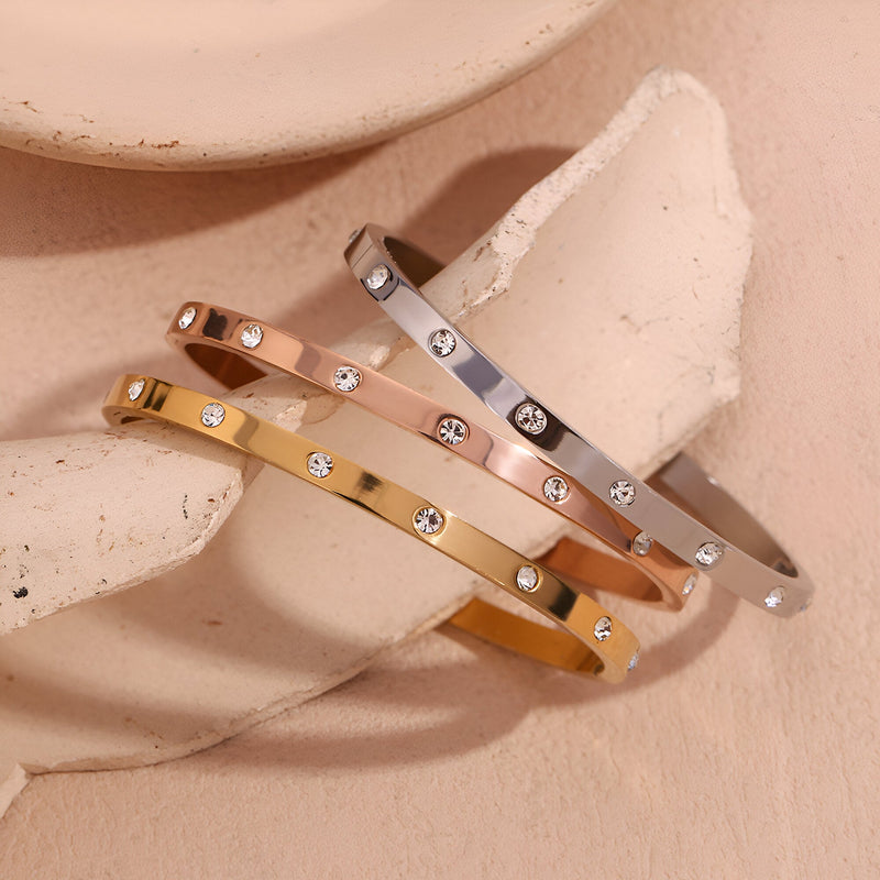 Bracelet jonc en acier inoxydable doré avec éclats de lumière incrustés et finition brillante.