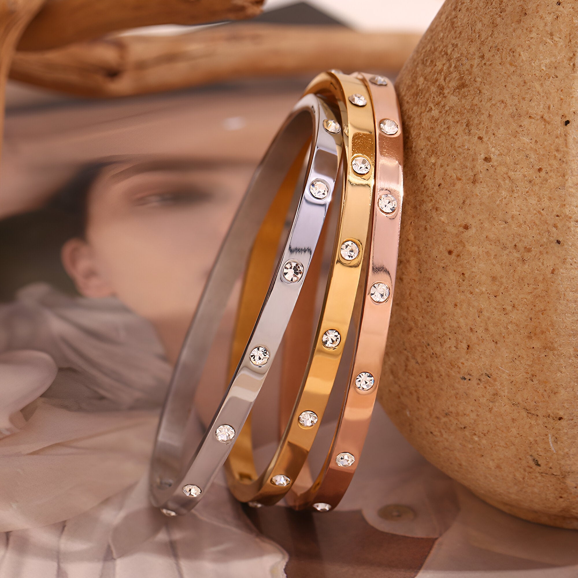 Trois bracelets joncs en acier inoxydable or, or rosé et argent avec éclats de lumière circulaires.