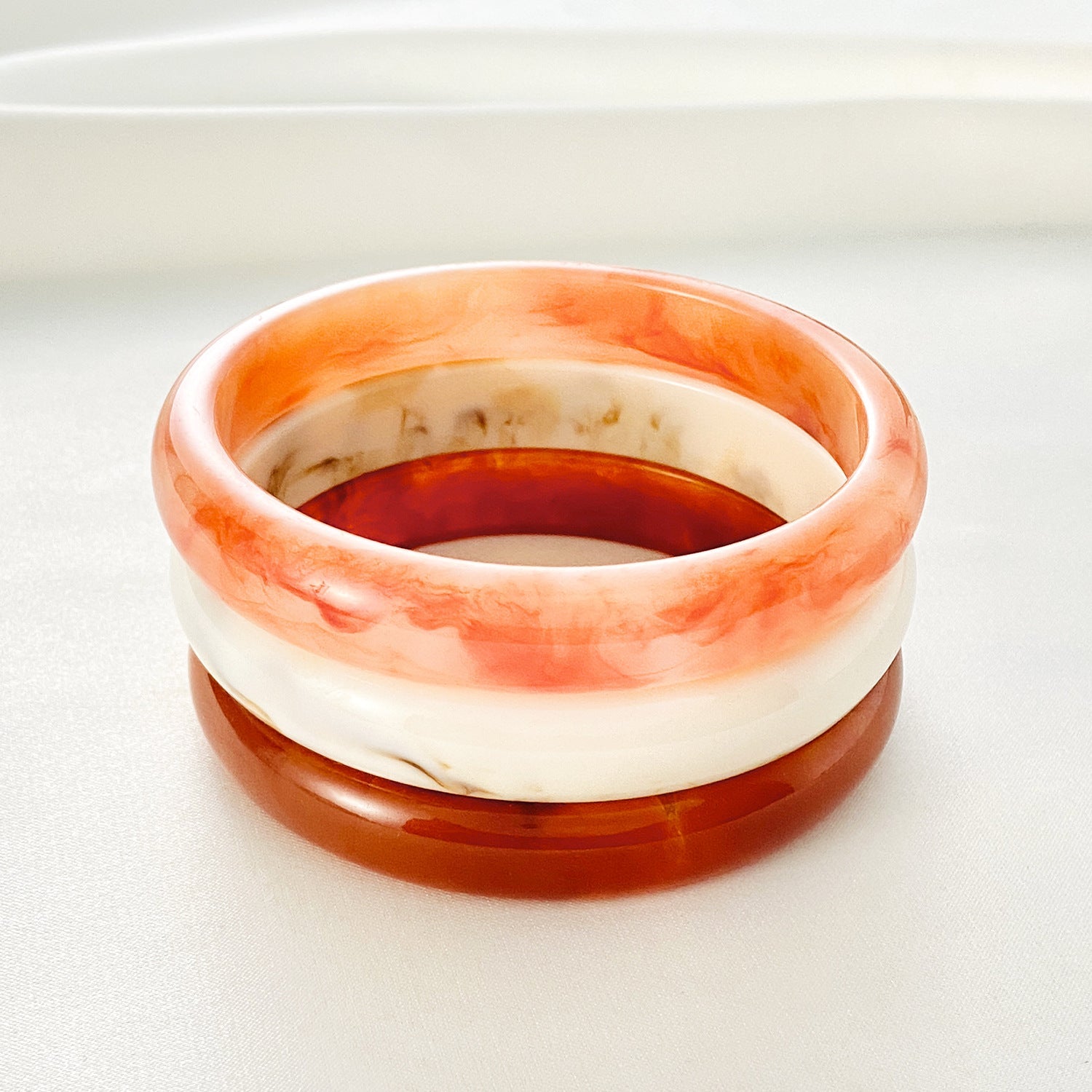 Bracelet jonc en acrylique avec effets marbrés orange clair, blanc cassé et marron profond, finition lisse et brillante.