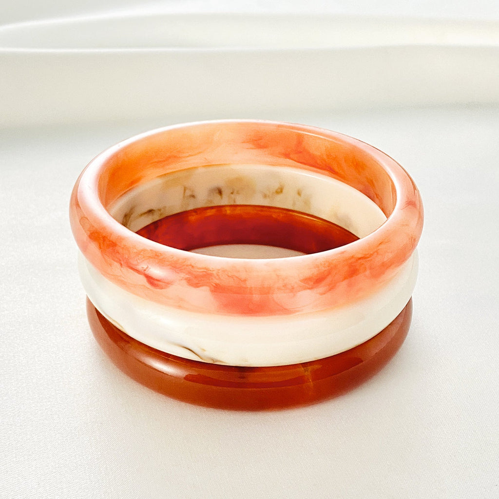 Bracelet jonc en acrylique avec effets marbrés orange clair, blanc cassé et marron profond, finition lisse et brillante.