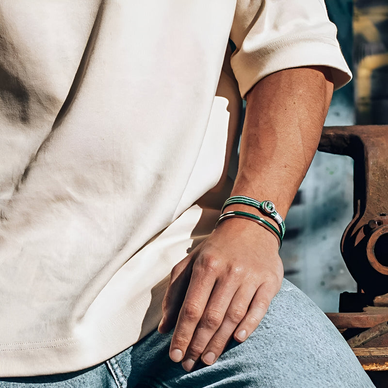 Bracelet jonc en acier inoxydable argent avec corde verte et fermoir noir porté au poignet homme.