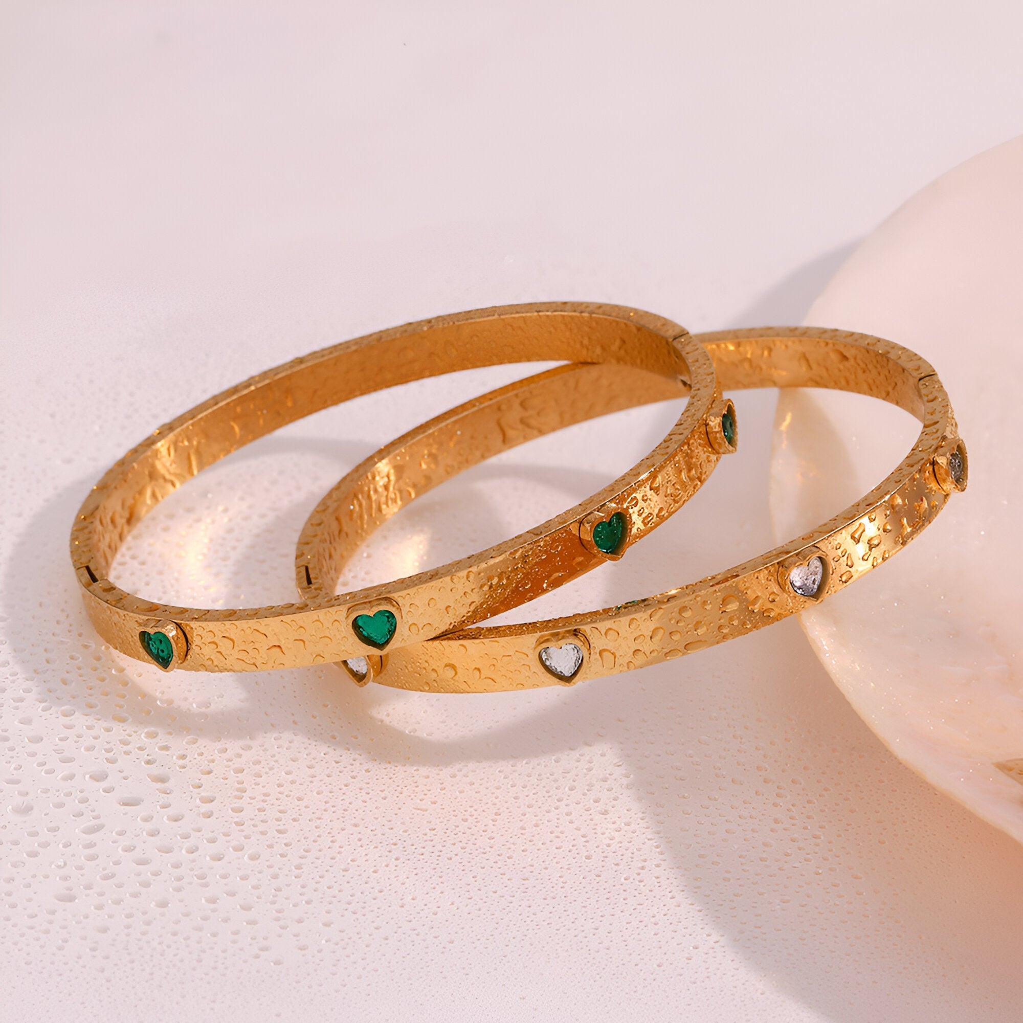 Bracelets joncs en acier plaqué or 18 carats avec petits cœurs verts et diamants, texture martelée.