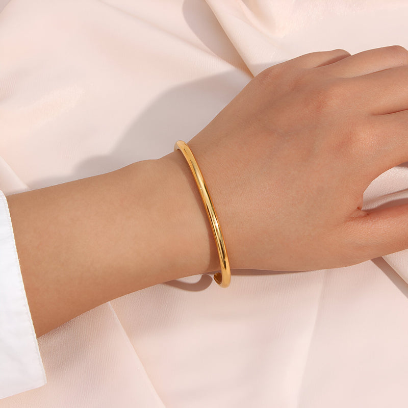 Bracelet jonc en acier inoxydable doré, finition lisse et design épuré porté au poignet féminin.