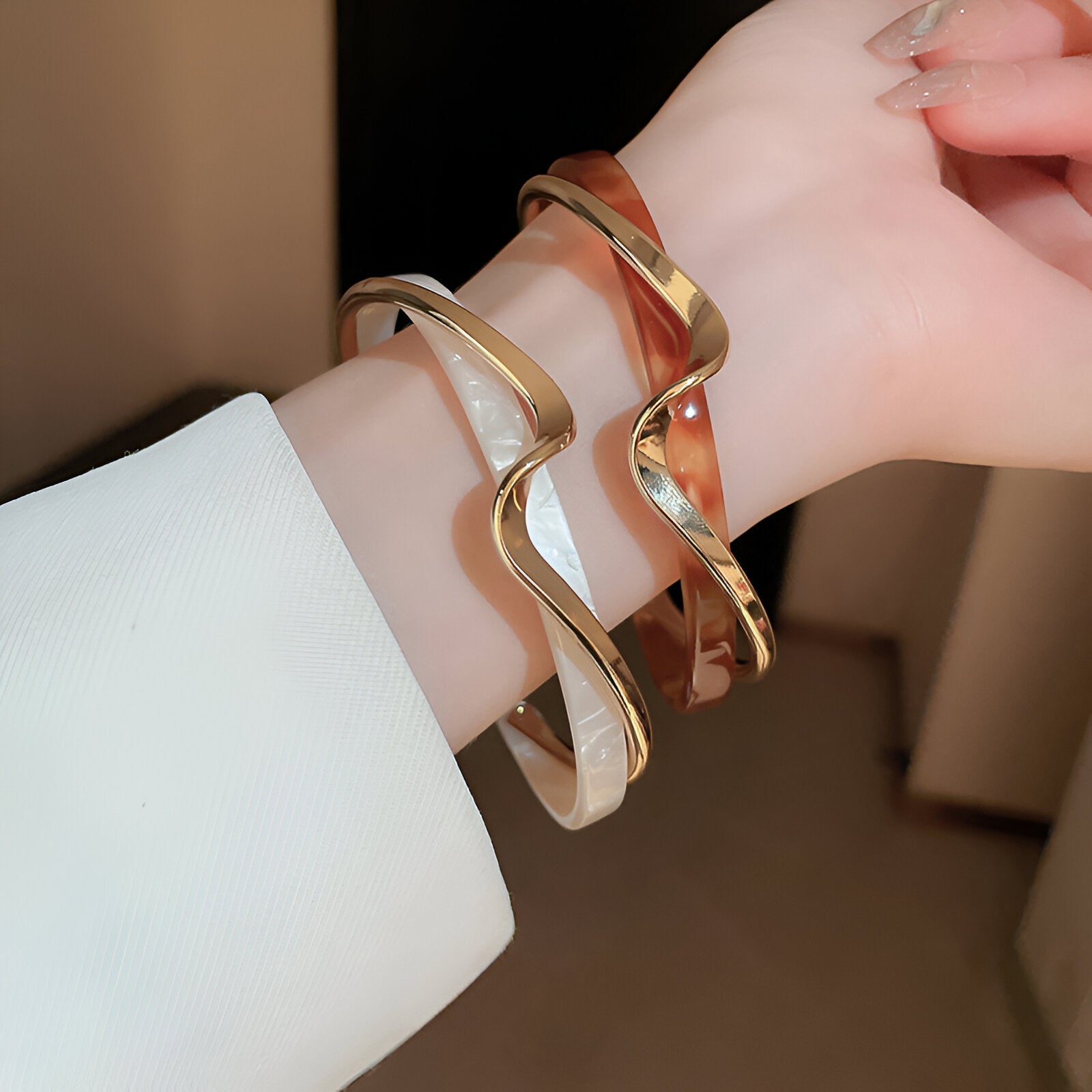 Bracelets jonc en acrylique blanc tacheté et métal doré, avec design ondulé élégant, portés sur poignet féminin.