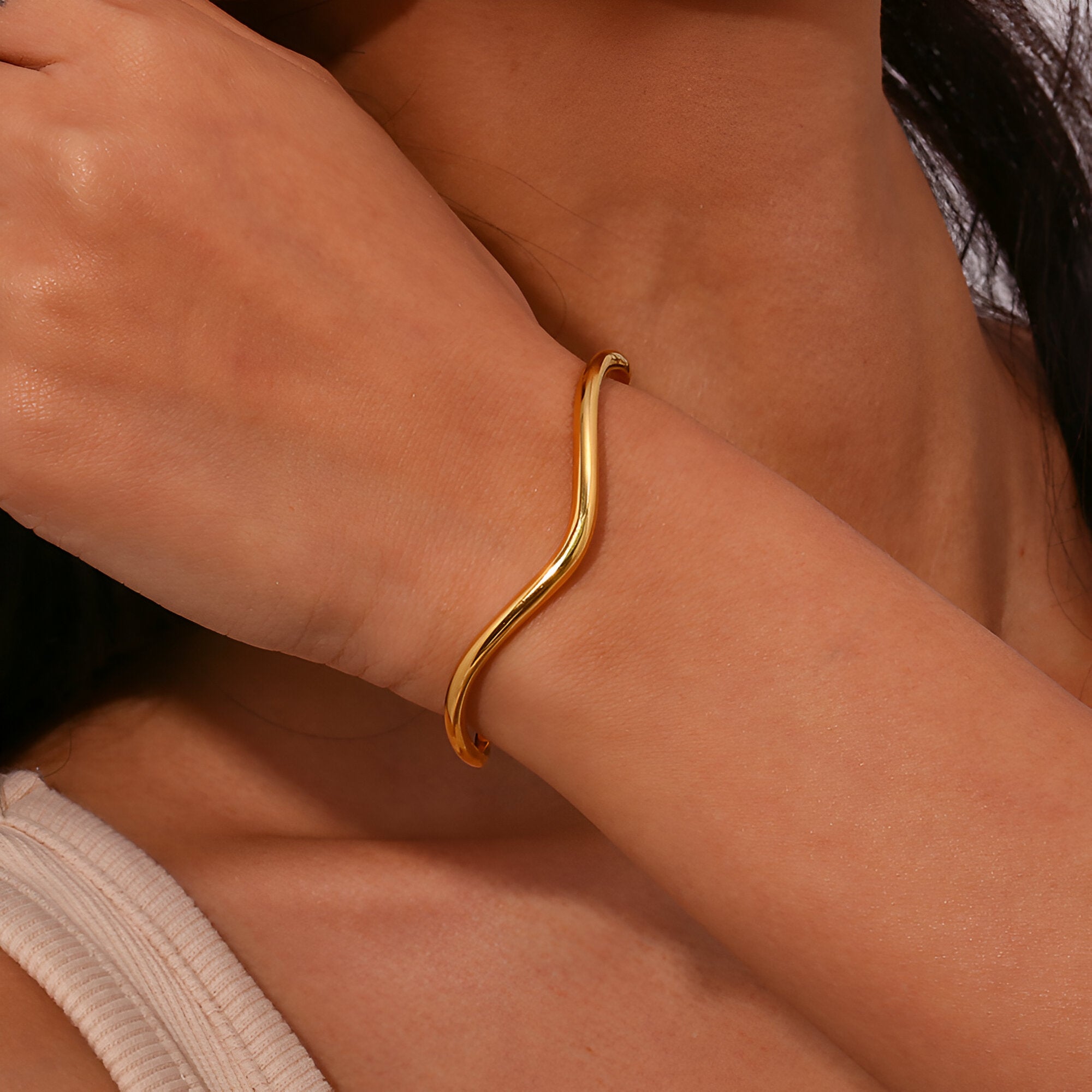 Bracelet jonc ondulé en acier inoxydable doré porté au poignet, design minimaliste et élégant.