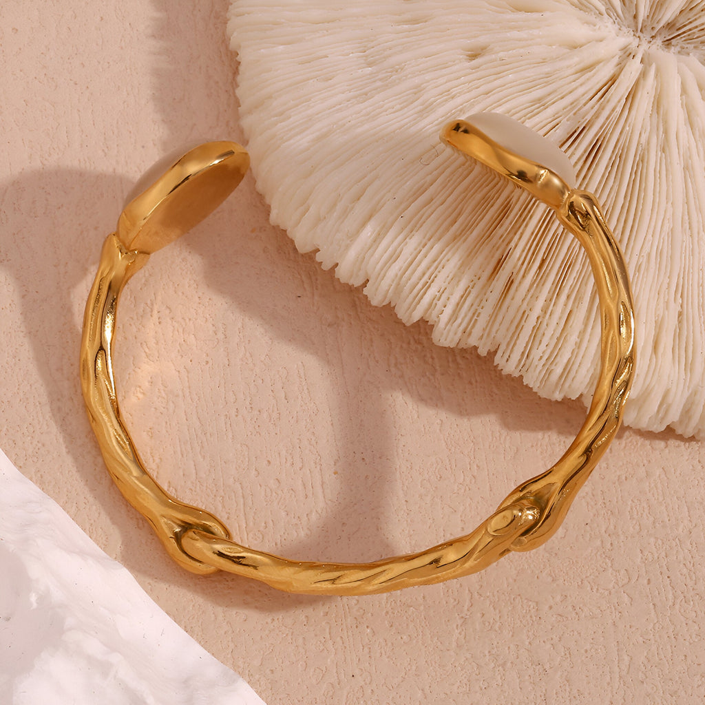 Bracelet jonc en acier inoxydable doré avec texture ondulée et fermoir ouvert.