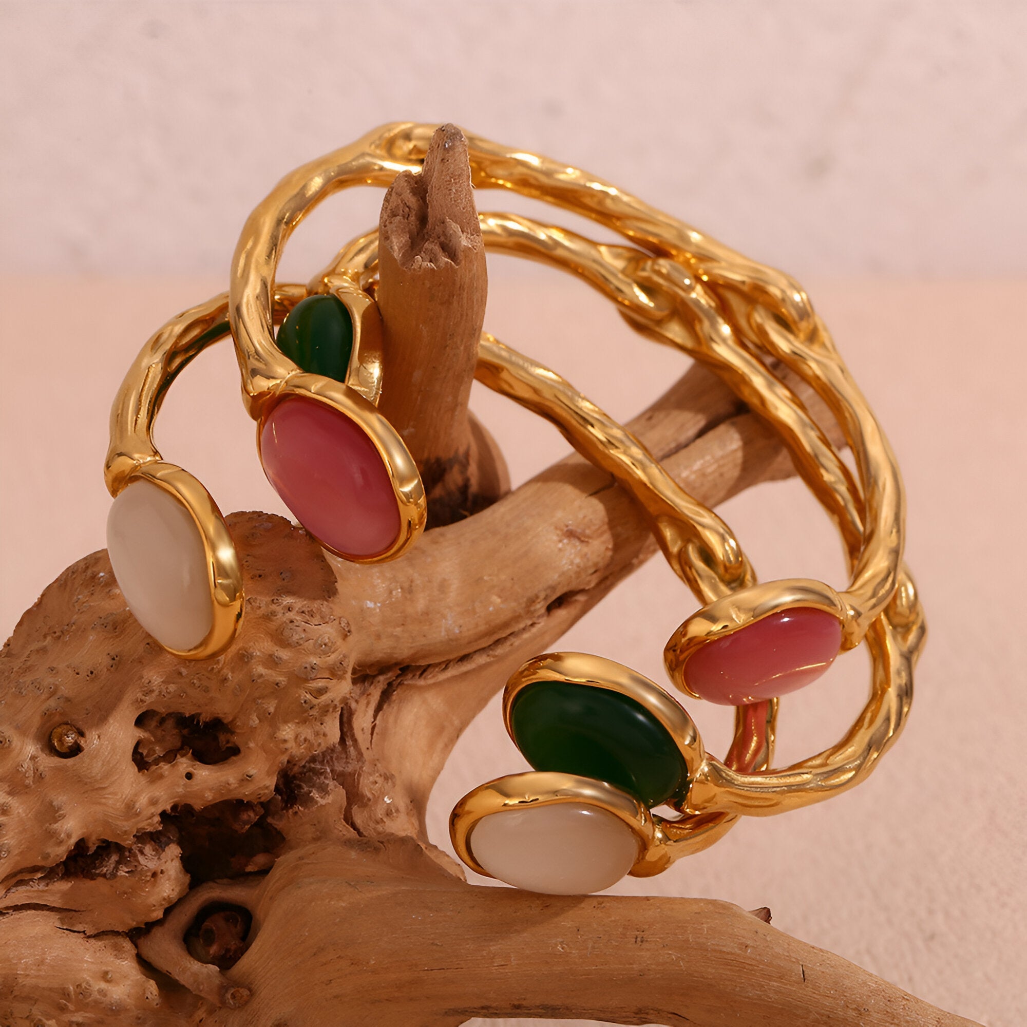 Bracelet jonc doré en acier inoxydable avec perles naturelles ovales vertes, roses et blanches sur bois naturel.