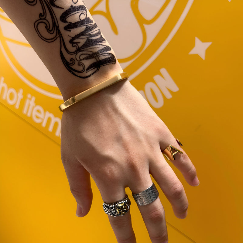 Bracelet jonc épuré en titane doré porté au poignet masculin avec trois bagues métalliques variées.