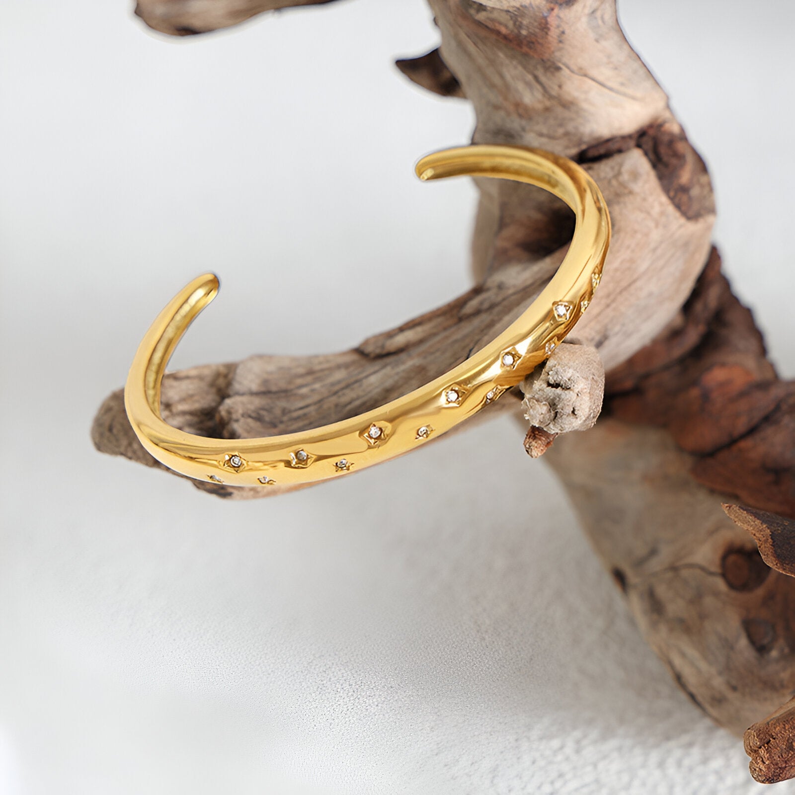 Bracelet jonc en titane plaqué or 18 carats avec zircons sertis, style Gabriella, posé sur bois clair.