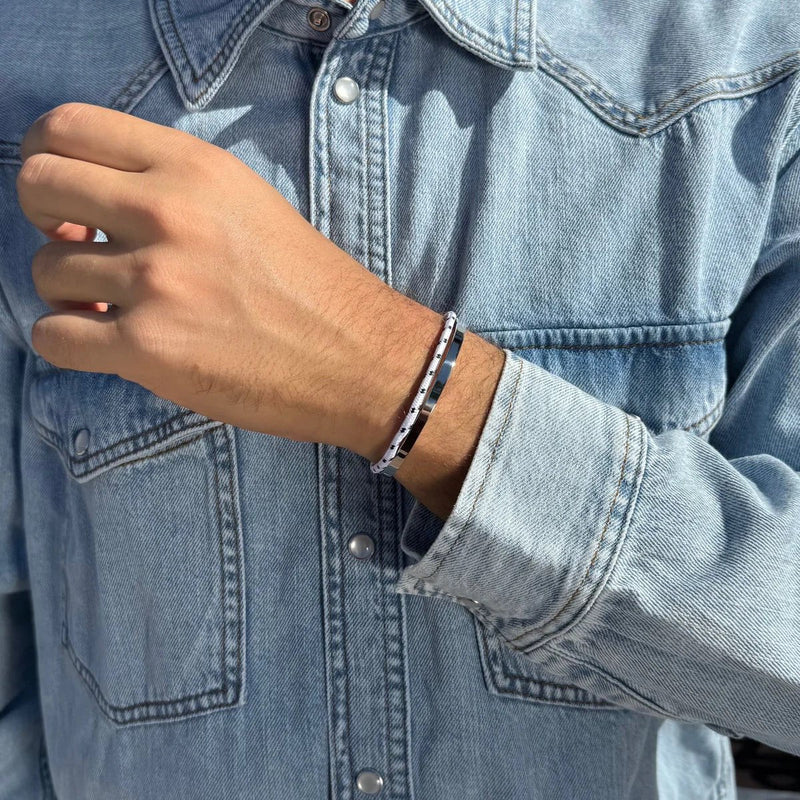 Bracelet jonc fin en acier inoxydable argenté avec cordon noir ajustable sur poignet masculin, porté avec une veste en jean.