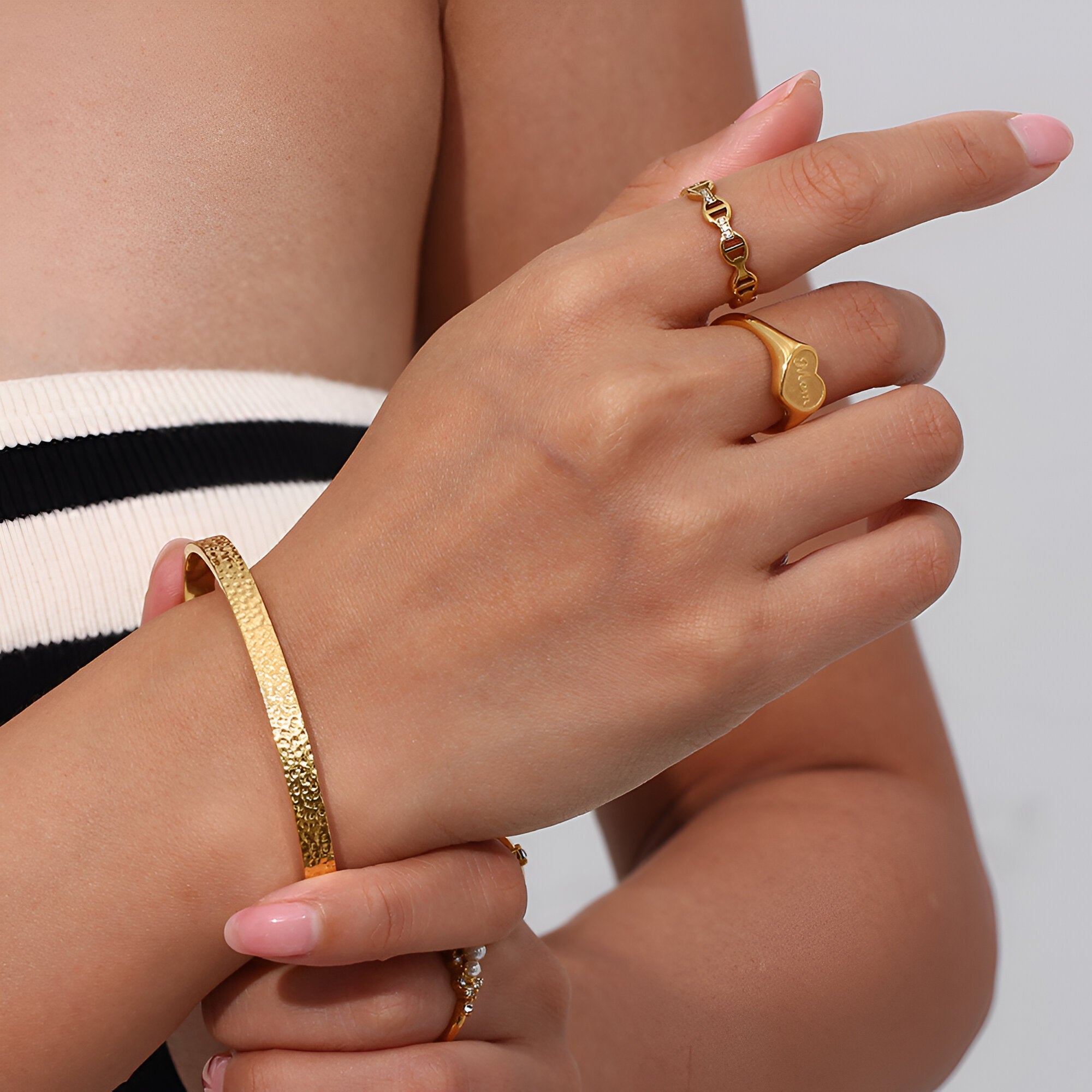 Bracelet jonc doré finition martelée en acier inoxydable porté au poignet féminin.