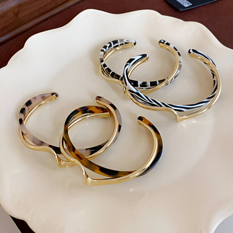 Quatre bracelets joncs en acrylique avec motifs léopard et zèbre, finition métal argenté et doré, posés sur une assiette.