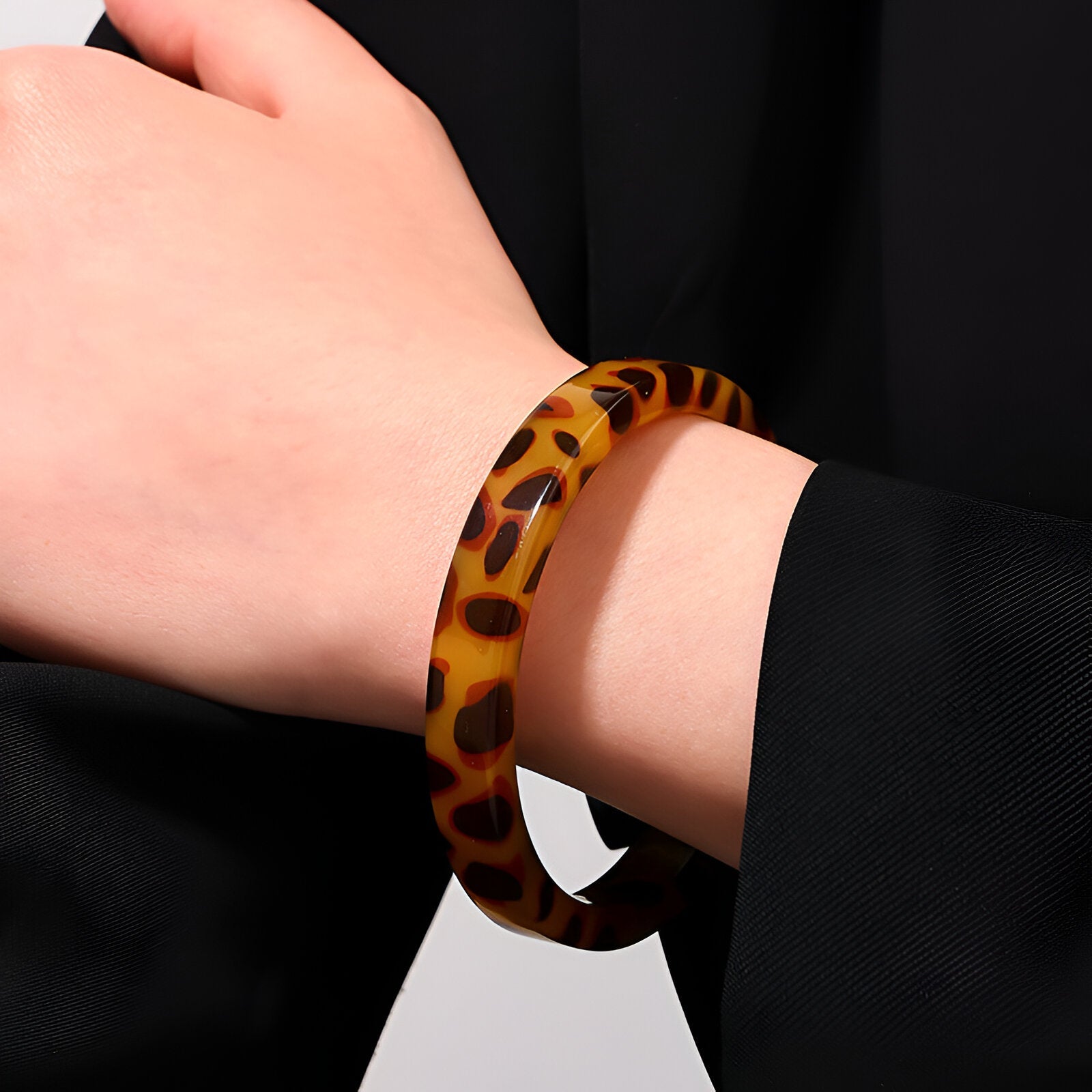 Bracelet jonc marron en acrylique avec motif léopard porté au poignet féminin.