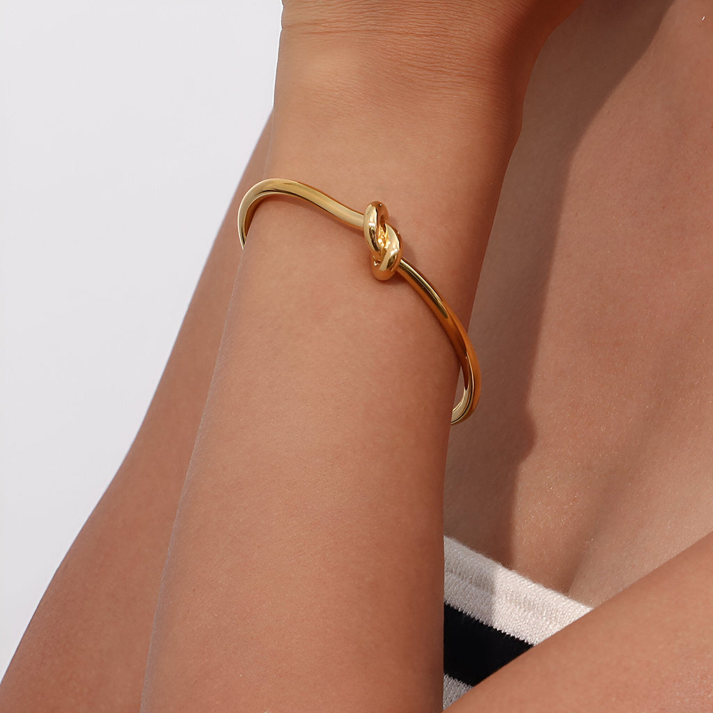 Bracelet jonc en acier inoxydable doré avec nœud élégant, style infini, porté au poignet féminin.