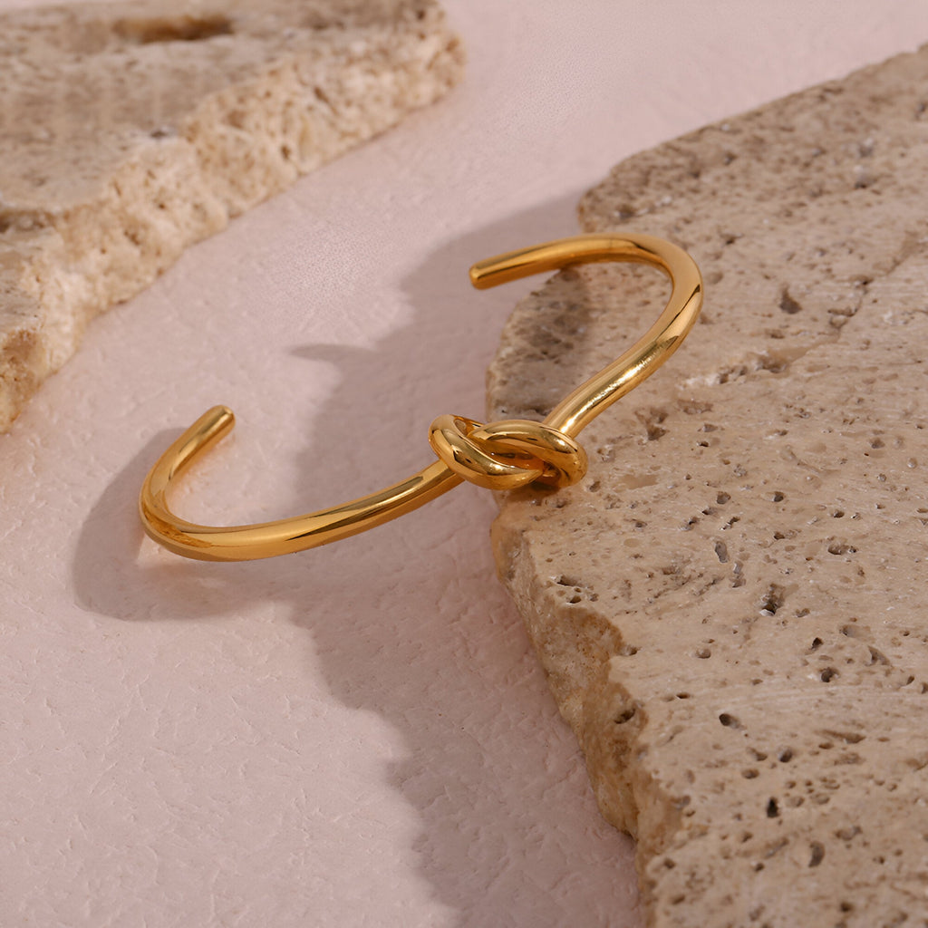 Bracelet jonc infini en acier inoxydable doré avec un noeud central élégant.