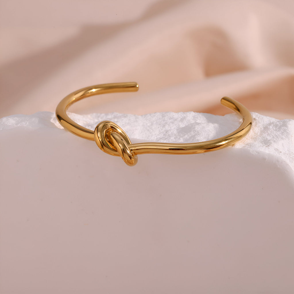 Bracelet jonc en acier inoxydable doré avec nœud central style infini élégant pour femme.