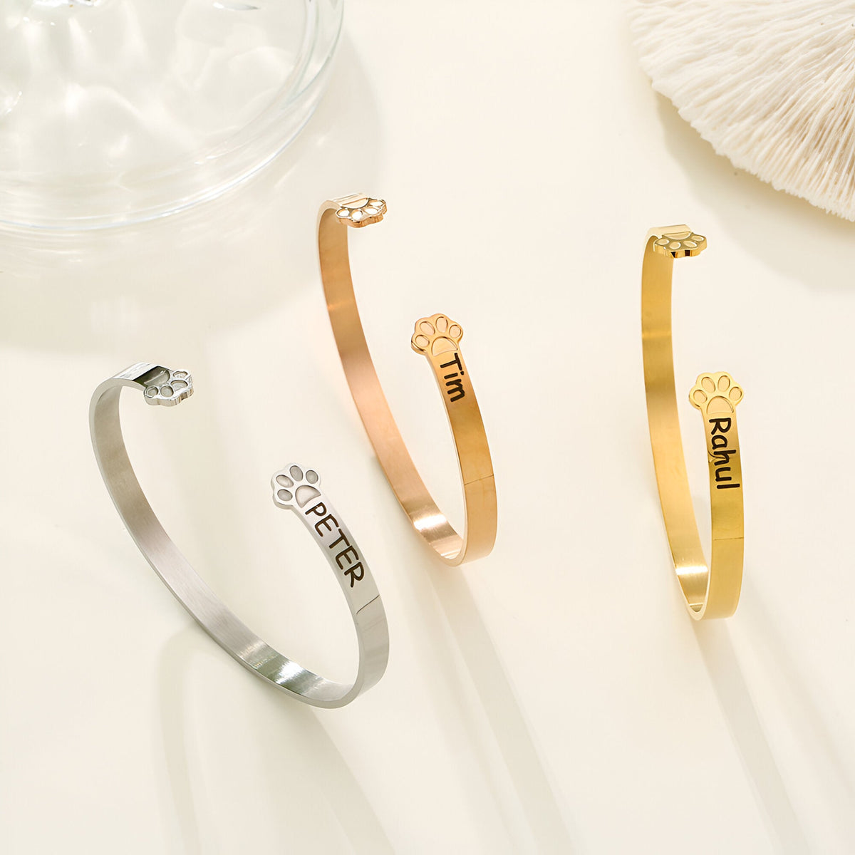 Trois bracelets joncs personnalisés en argent, or rosé et or avec patte d'animal gravée et noms différents.