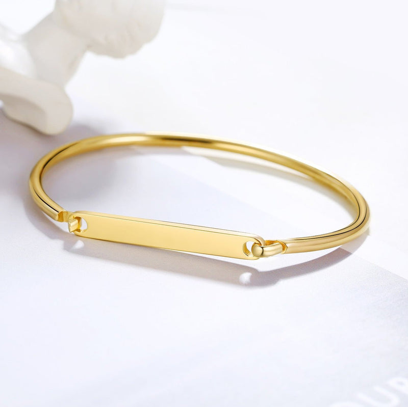Bracelet jonc en acier inoxydable doré avec plaque personnalisable lisse et fermoir minimaliste.