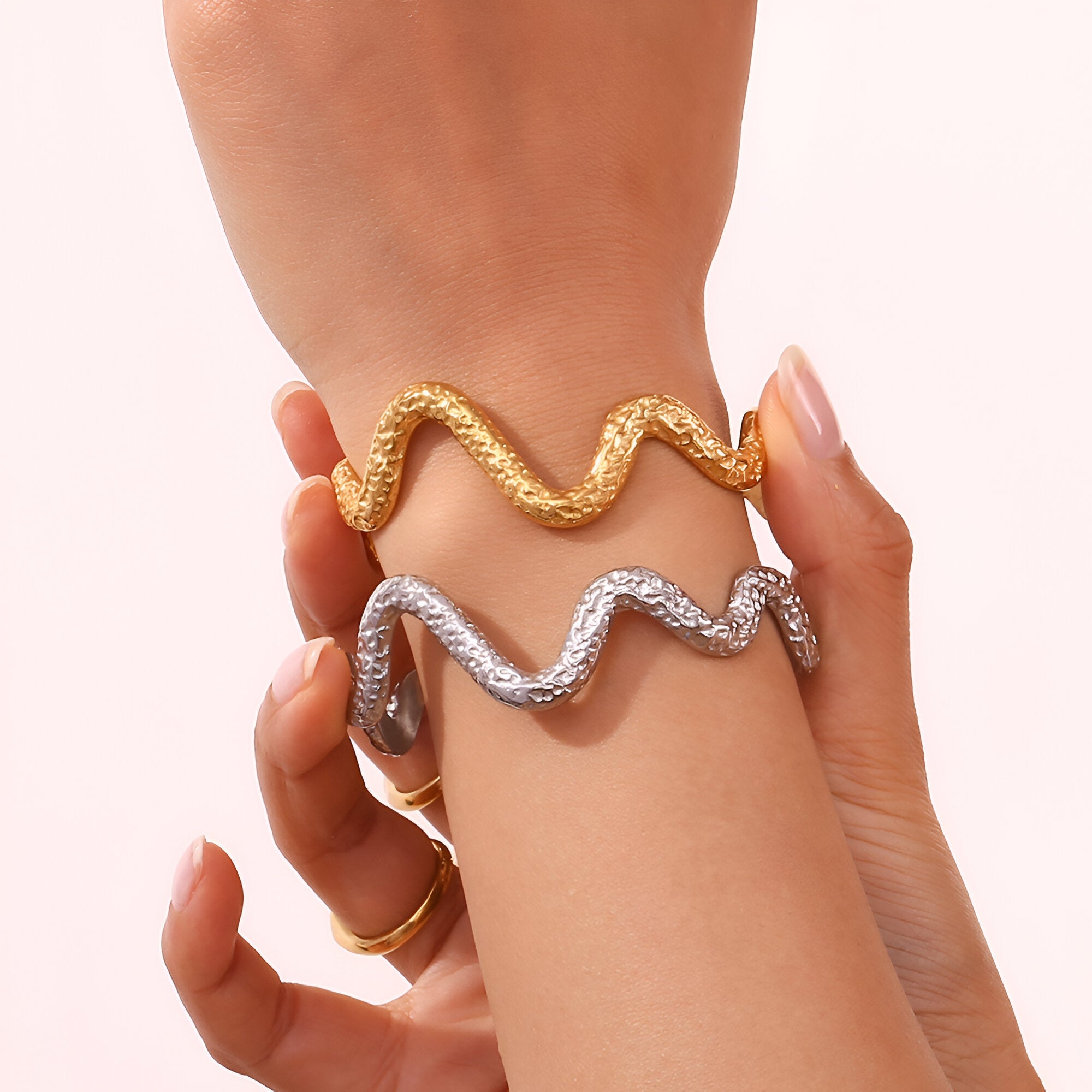 Bracelet jonc serpentine en acier inoxydable doré et argenté porté au poignet, motifs ondulés texturés.