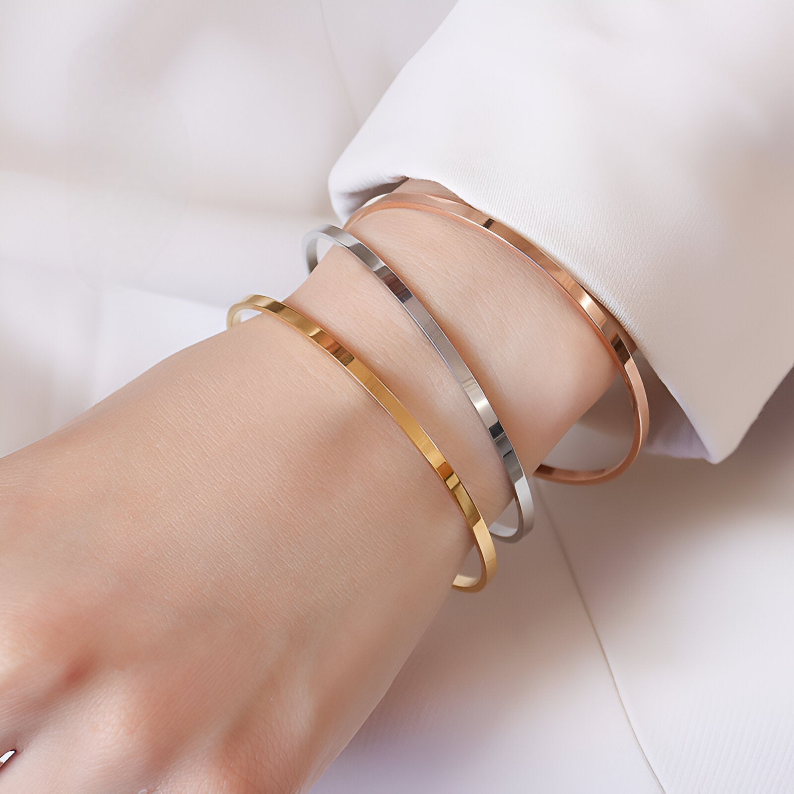 Trois bracelets joncs fins en titane plaqué or jaune, argent, et or rosé, modèle Twila, portés au poignet.