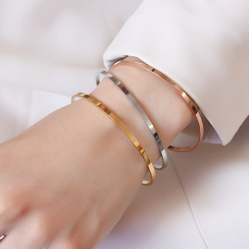 Trois bracelets joncs fins en titane plaqué or jaune, argent, et or rosé, modèle Twila, portés au poignet.