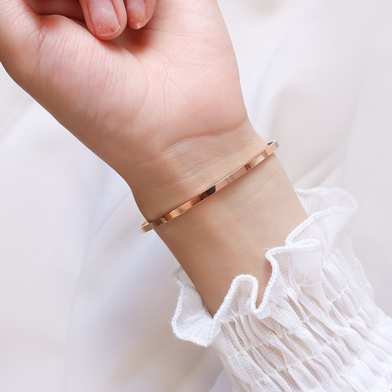 Bracelet jonc fin en titane plaqué or 18 carats, finition lisse et brillante, porté au poignet féminin.