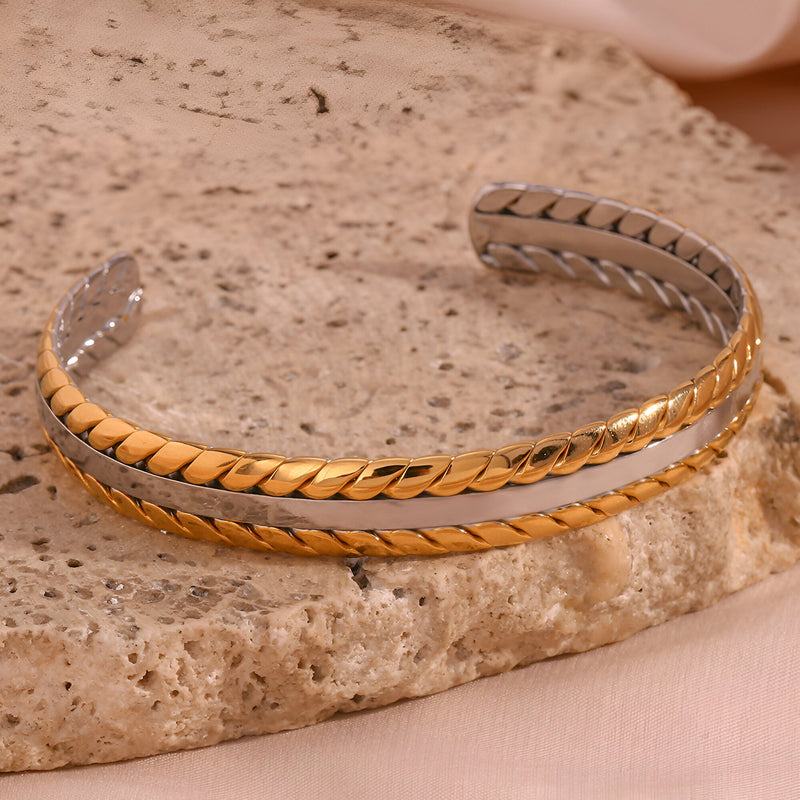 Bracelet jonc fin en acier inoxydable plaqué or avec tressage délicat sur pierre beige.
