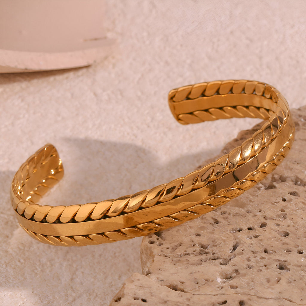 Bracelet jonc en acier inoxydable plaqué or avec tressage délicat et finition brillante.