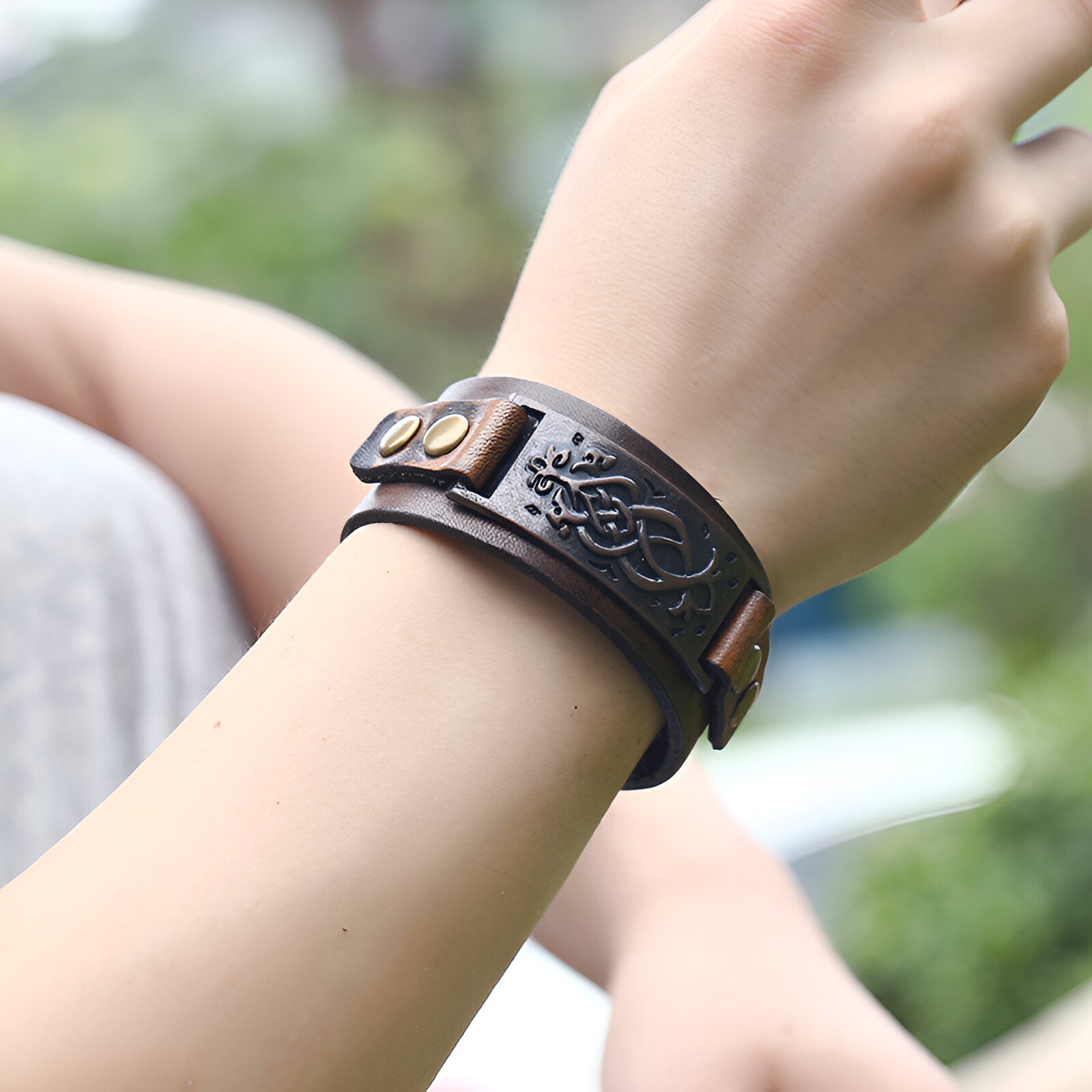 Bracelet large en cuir marron à motif floral embossé avec boucle à rivets métalliques.