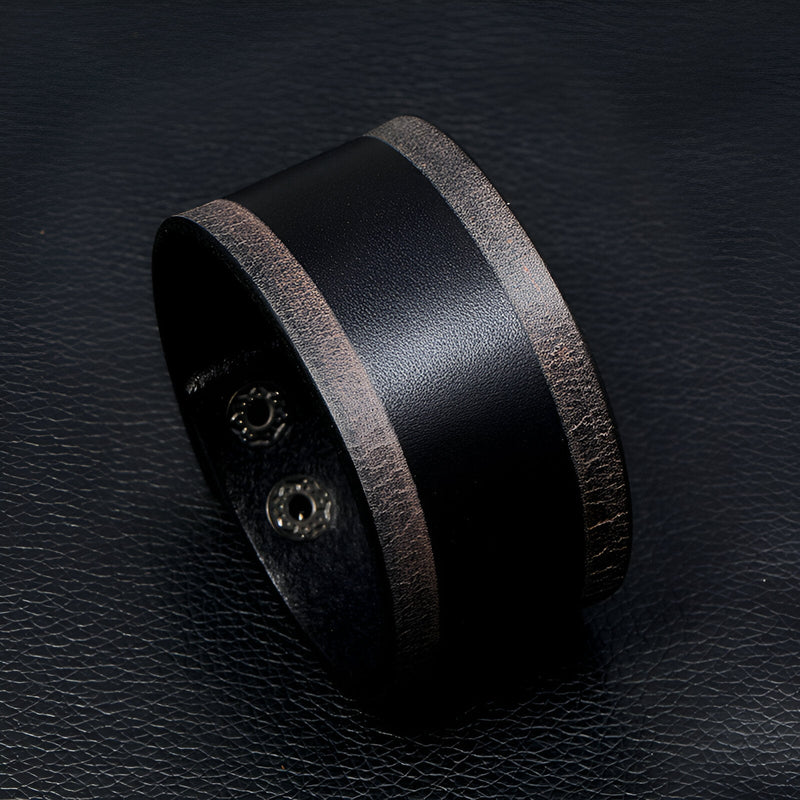 Bracelet large en cuir noir avec bords marron vintage et fermeture à pression métallique.