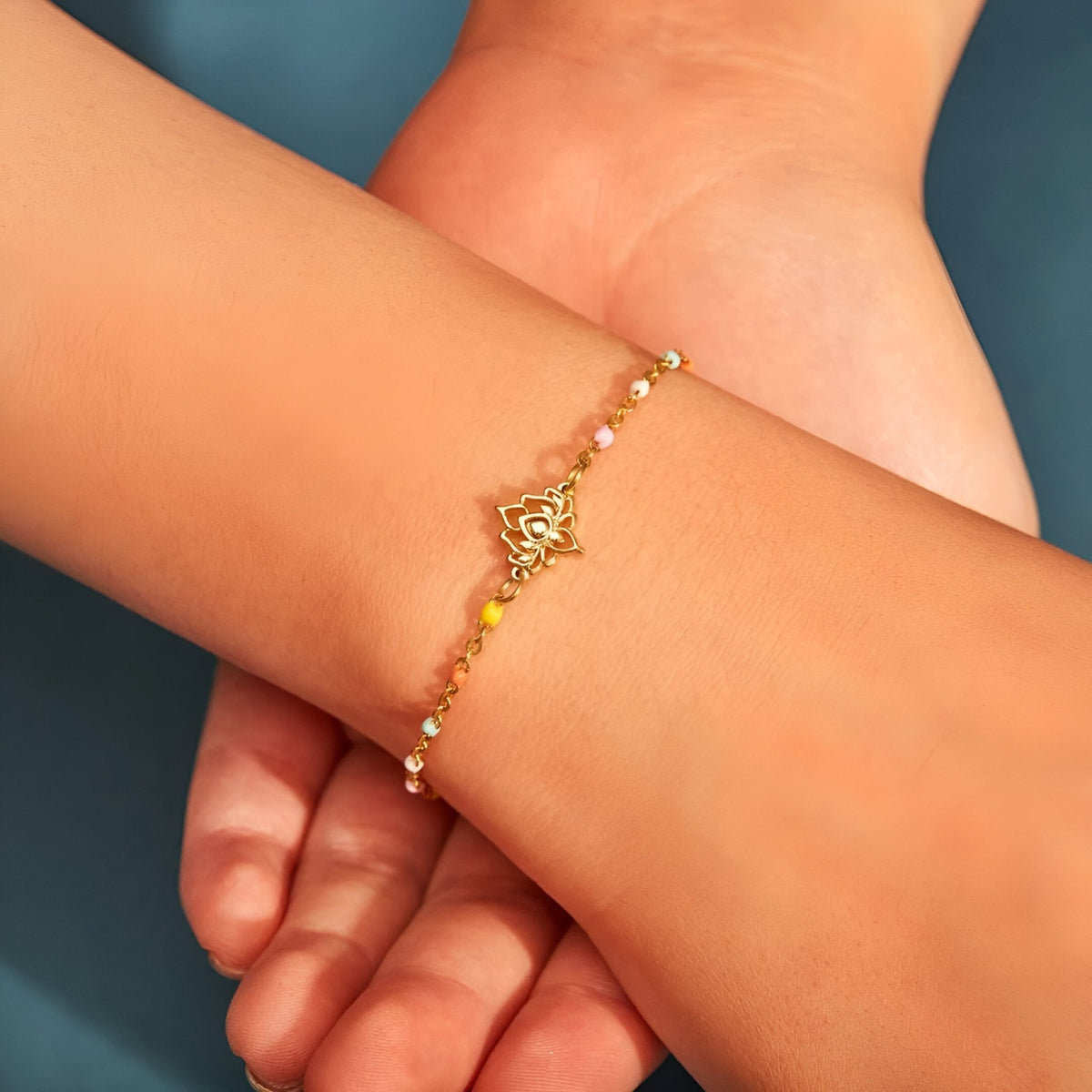Bracelet fin en argent doré avec pendentif lotus ajouré et perles roses et dorées.