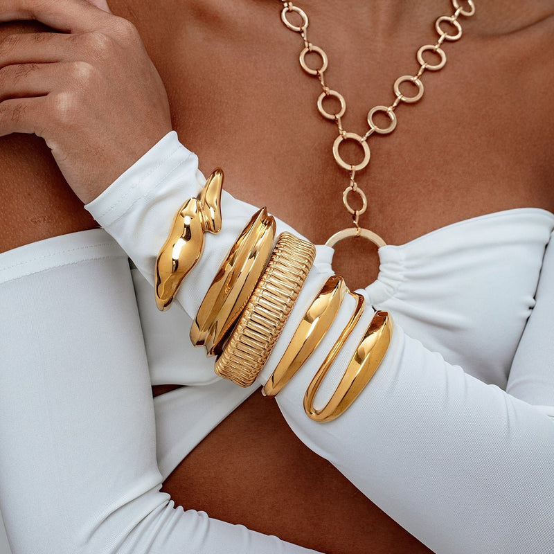 Bracelet manchette doré texturé en acier inoxydable, forme large et moderne, porté sur le poignet.