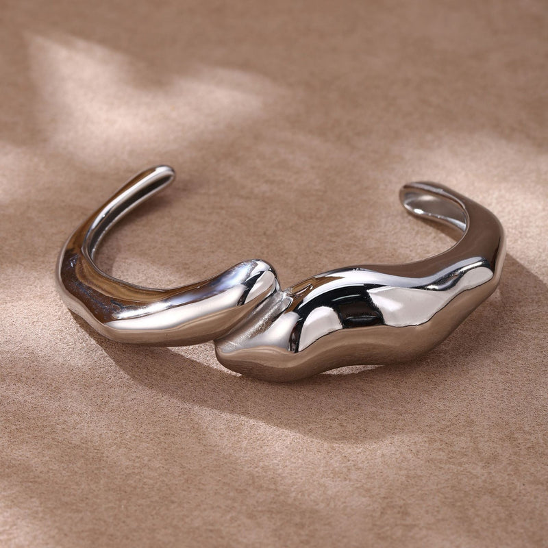 Bracelet manchette en acier inoxydable argenté avec finition lisse et design ondulé fondu.
