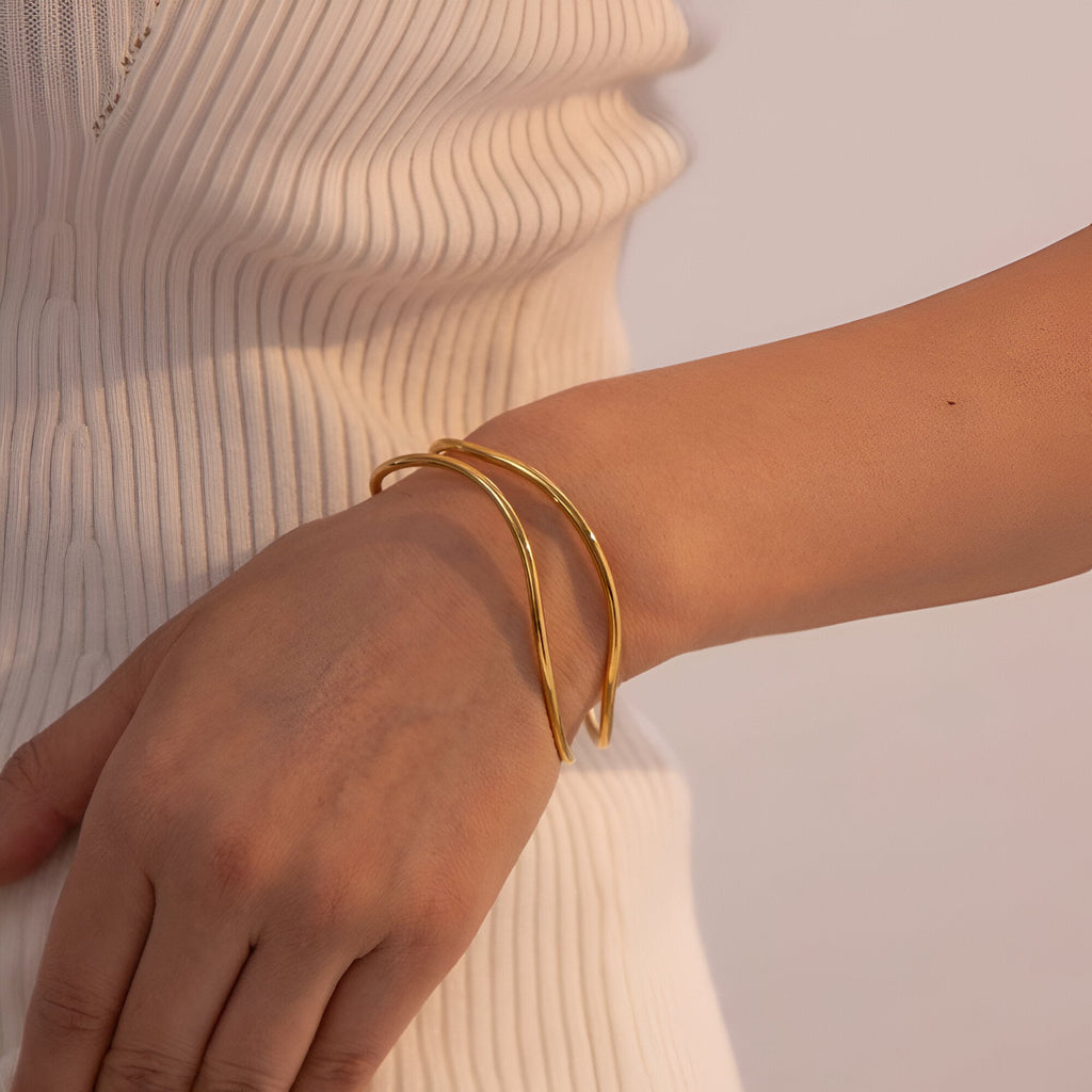 Bracelet manchette fin en titane plaqué or, design torsadé élégant sur poignet féminin.