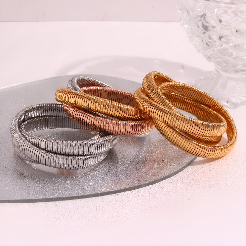 Ensemble de trois bracelets manchettes torsadés en argent, cuivre et or posés sur un plateau argenté.