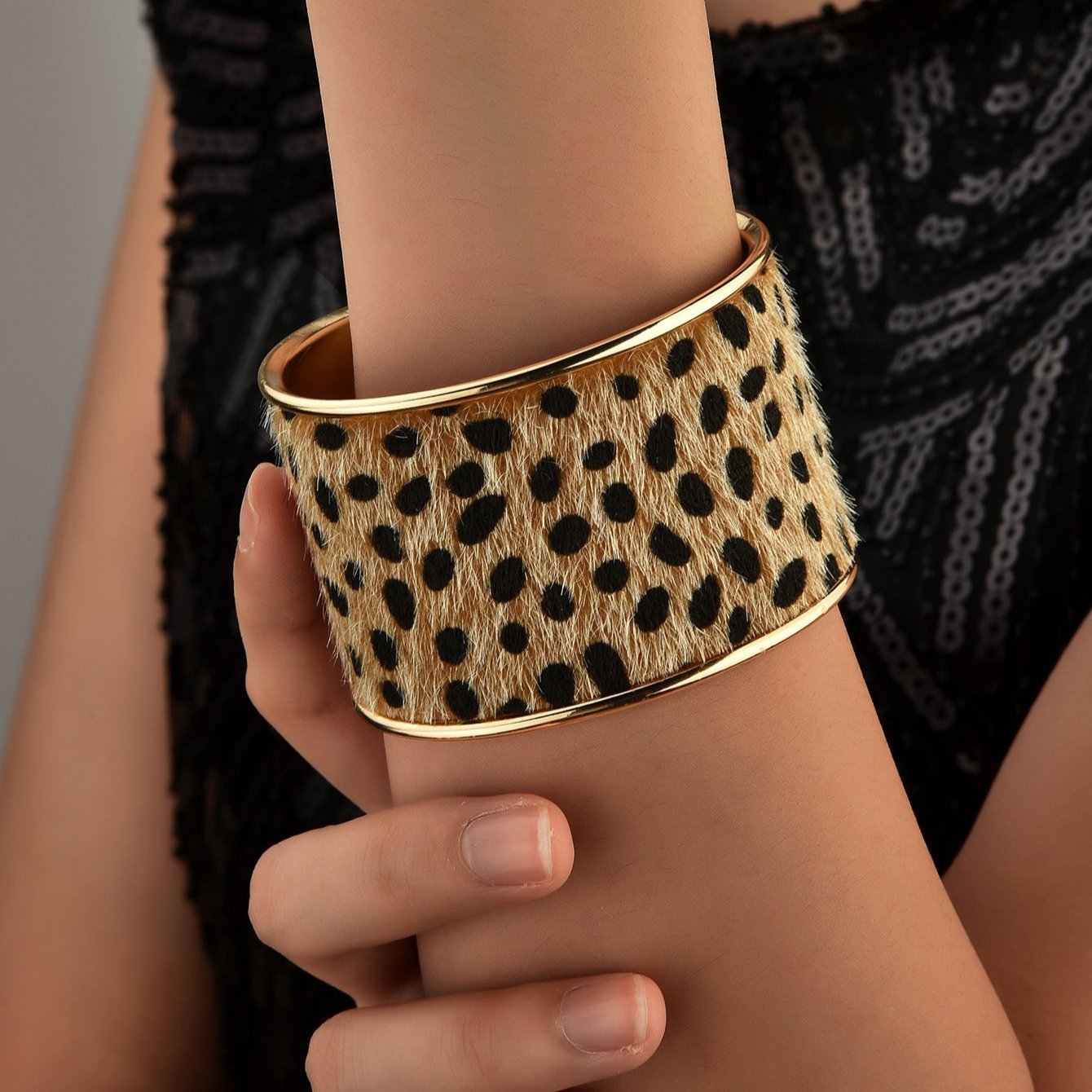 Bracelet manchette large en cuir imprimé léopard avec bord doré, porté au poignet femme.