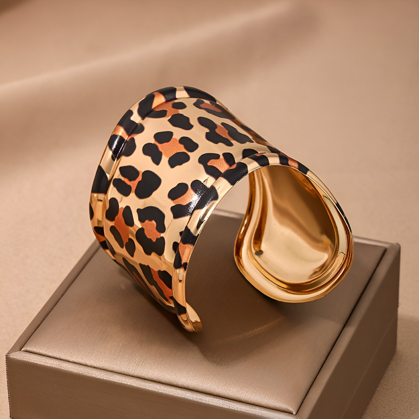 Bracelet manchette large en métal doré avec motif léopard noir et beige, finition brillante.