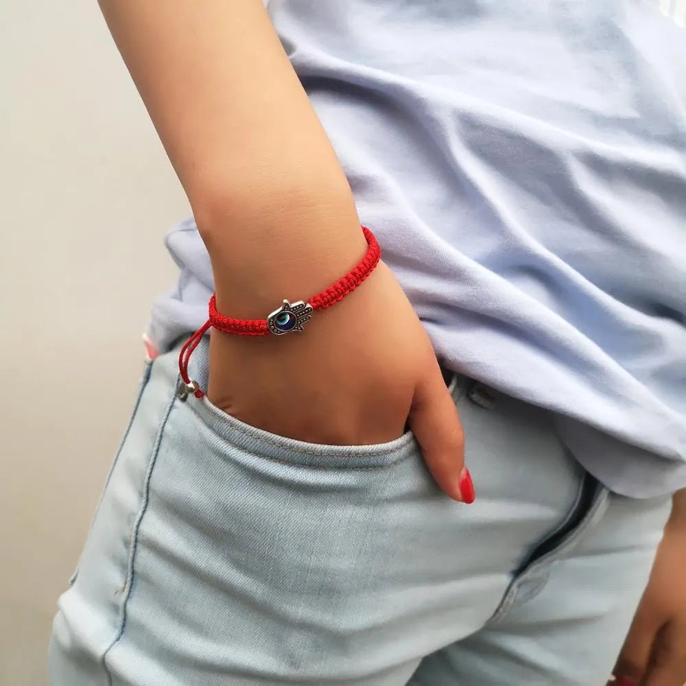 Bracelet rouge en fil ciré avec pendentifs œil protecteur bleu et main de Fatma argentée, porté au poignet.