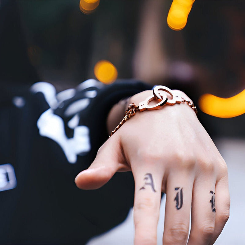 Bracelet menottes en acier inoxydable or rosé avec chaîne fine et fermoir stylisé.