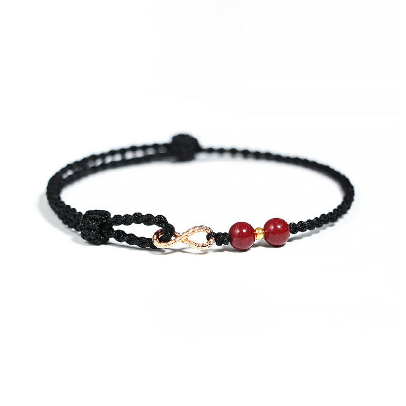 Bracelet fin en fil ciré noir avec deux pierres rouges de cinabre et un motif infini doré.