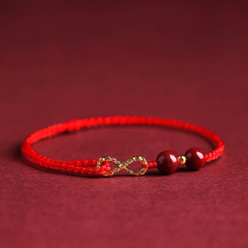 Bracelet rouge en fil ciré avec motif infini doré et deux pierres rouges de cinabre.