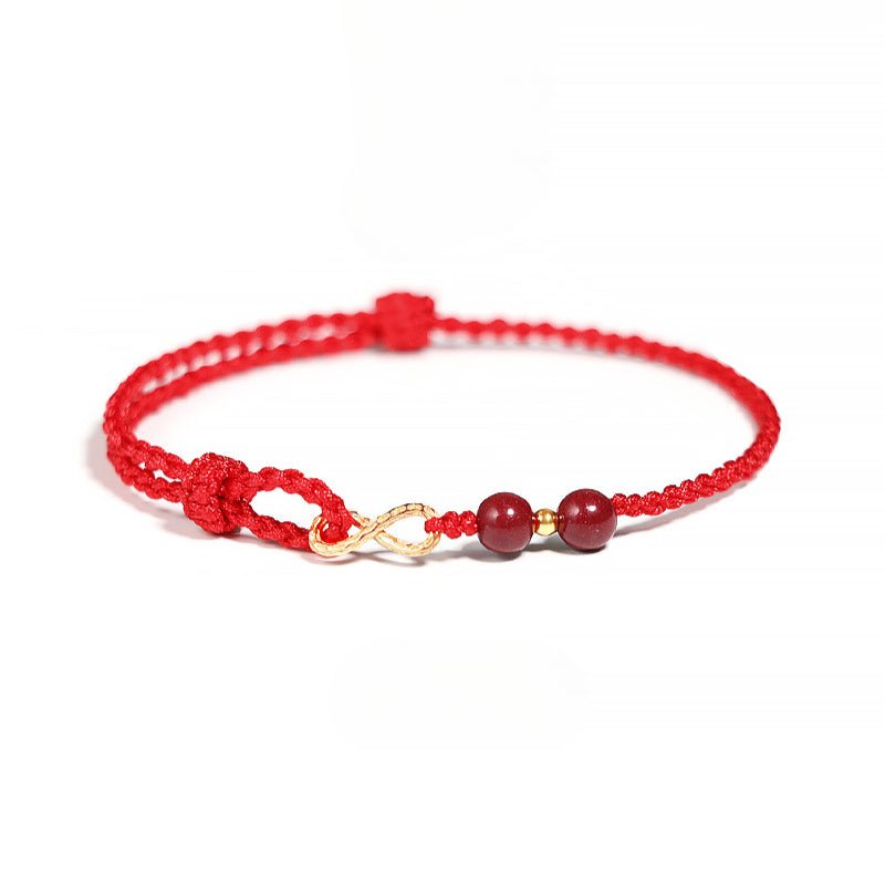 Bracelet minimaliste rouge en fil ciré avec motif infini doré et deux pierres de cinabre rondes.