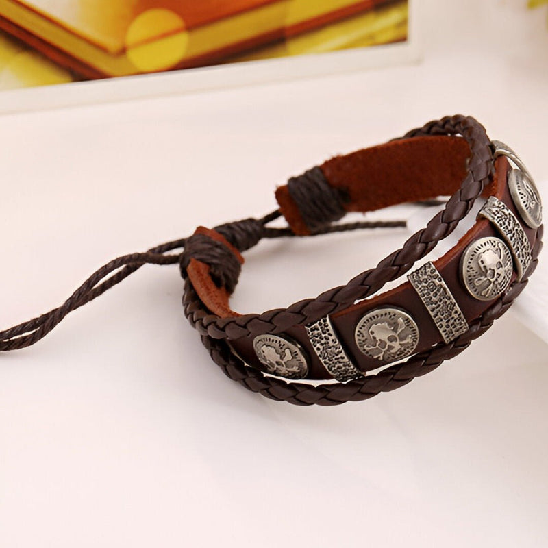 Bracelet multi-rangs en cuir marron avec têtes de mort argentées et tresse décorative.
