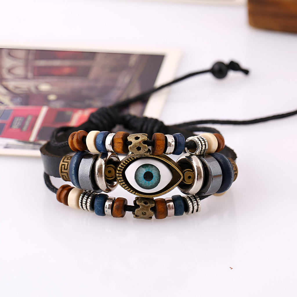 Bracelet multi-rangs en cuir noir et marron avec perles boisées et œil protecteur bleu au centre.
