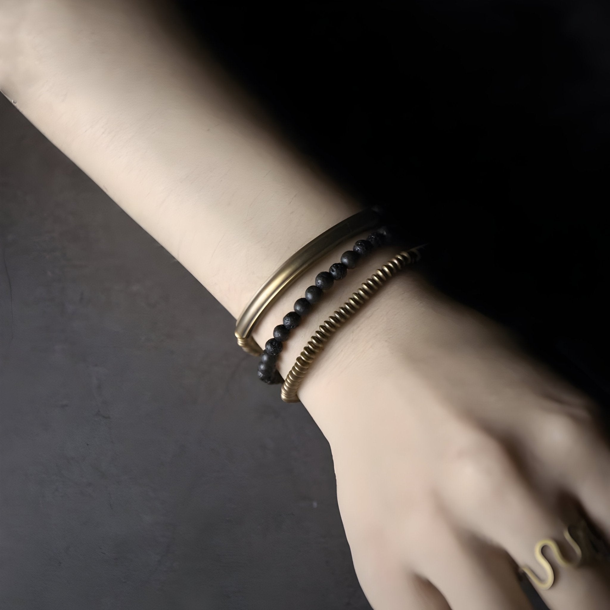 Bracelet multi-rangs cuivre mat et pierres volcaniques noires sur poignet pâle.