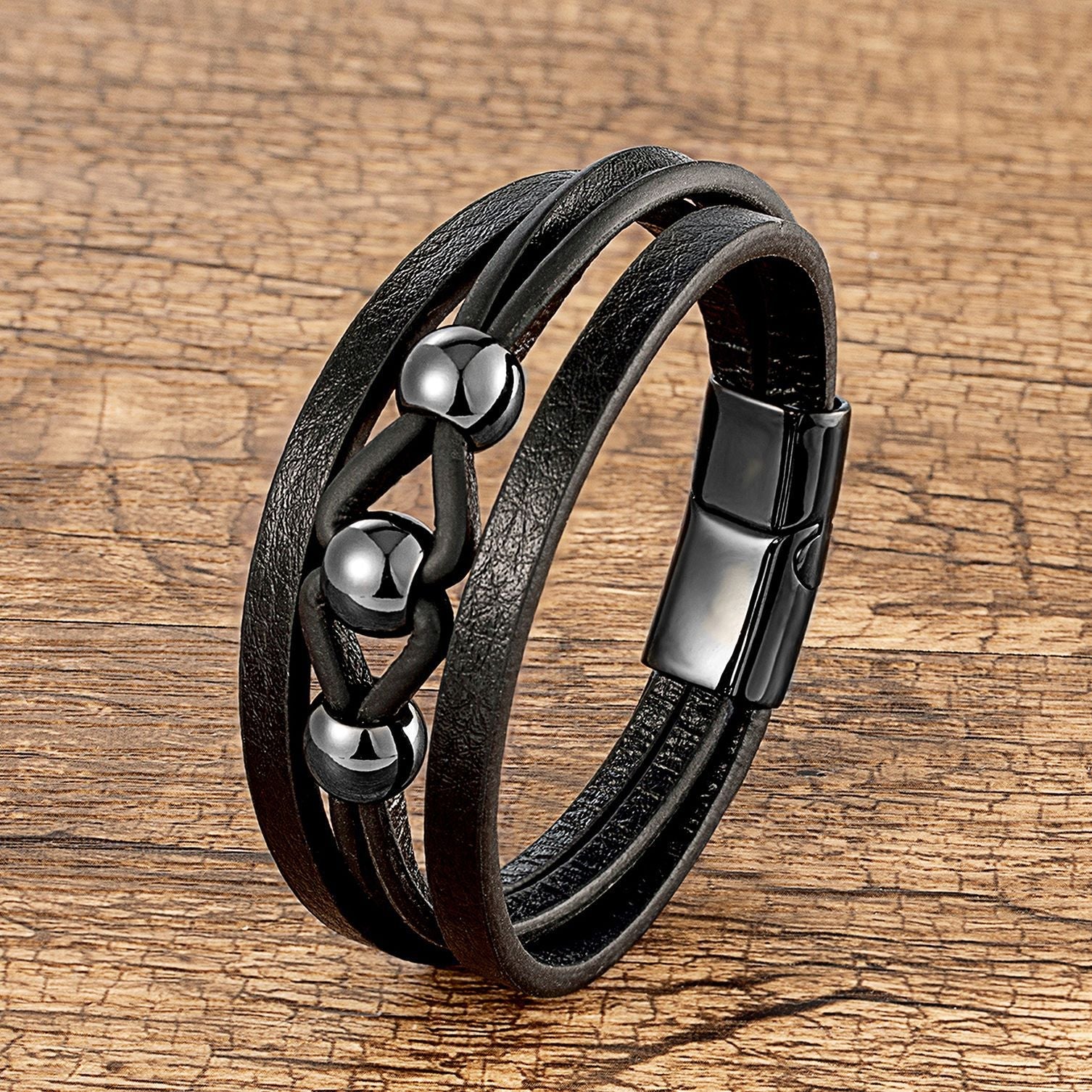 Bracelet multi-rangs en microfibre noir avec breloques métalliques argentées et fermoir magnétique noir.