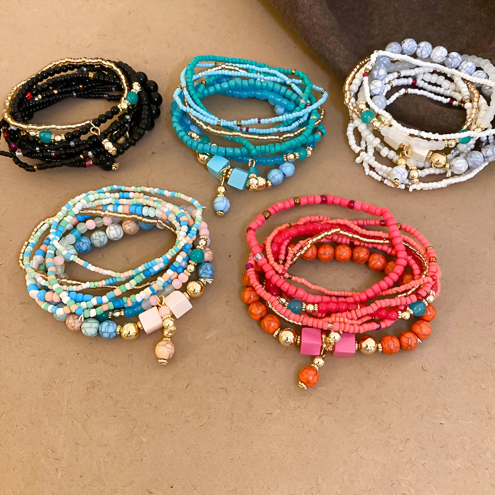 Bracelets multi-rangs en perles de résine élastique, couleurs noir, bleu, blanc, beige et rose avec pampilles dorées.