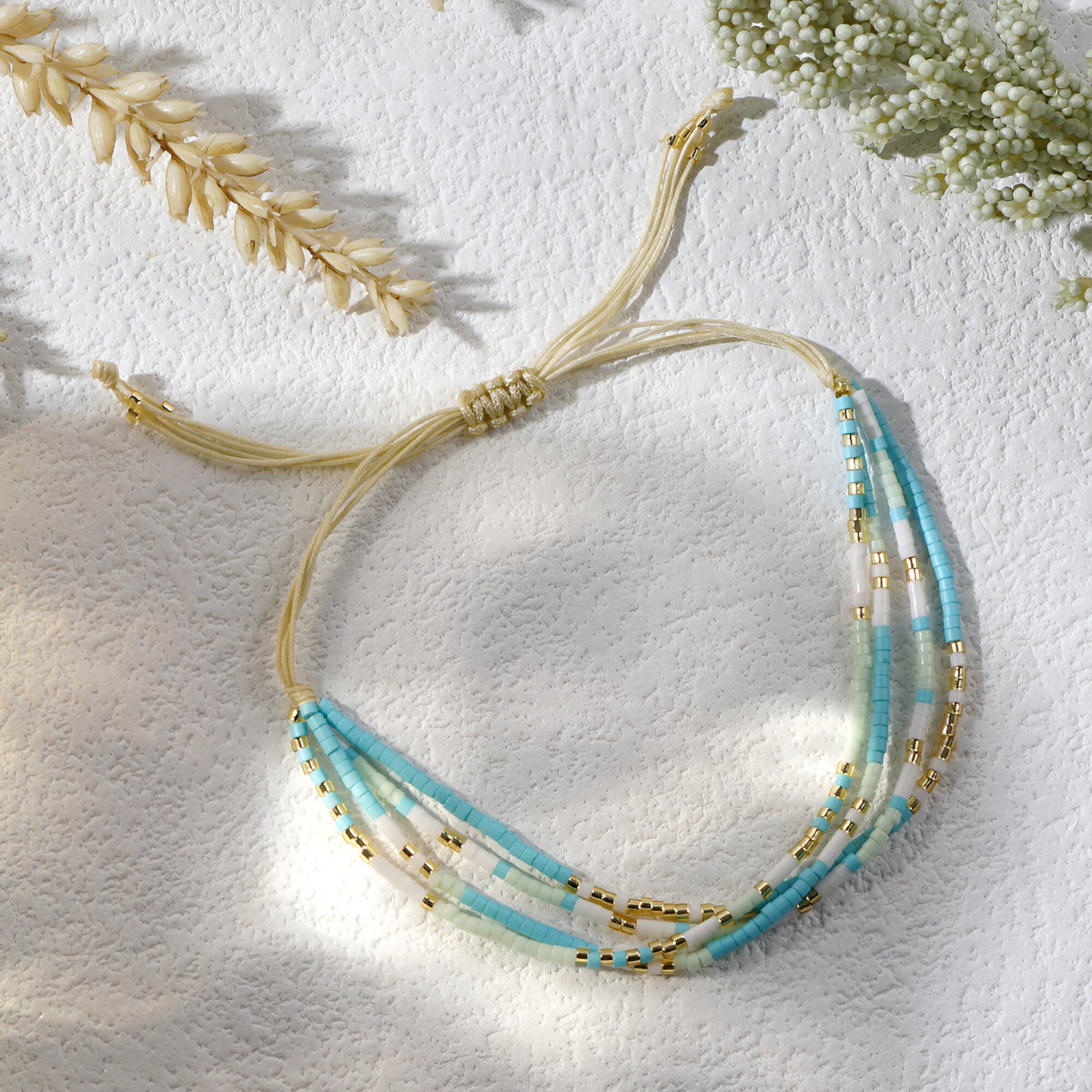 Bracelet multi-rangs en perles heishi bleu clair et doré sur cordon beige ajustable.